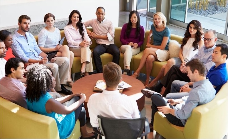 A group of people from diverse backgrounds sit around a table and share their personal experience with speaking English as an additional language.