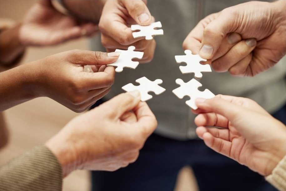 Five hands in a circle, each holding a puzzle piece.