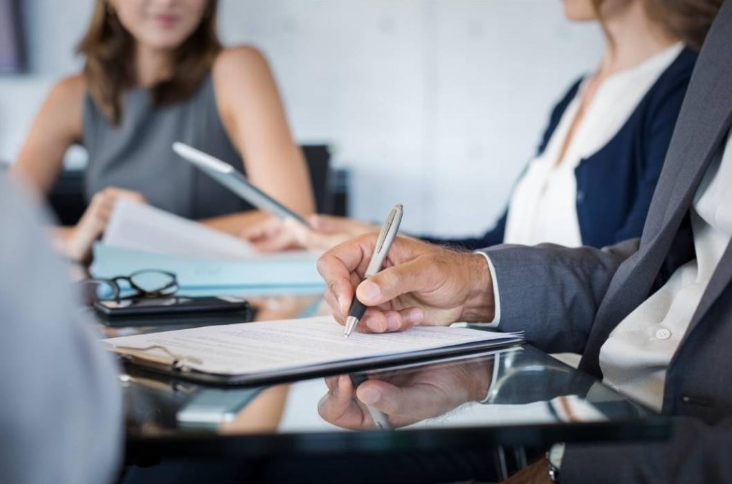 Three people sitting in a meething while one person takes notes.