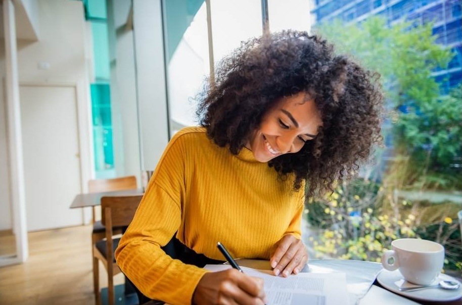 A woman sitting at a table with a cup of coffee, happily studying.