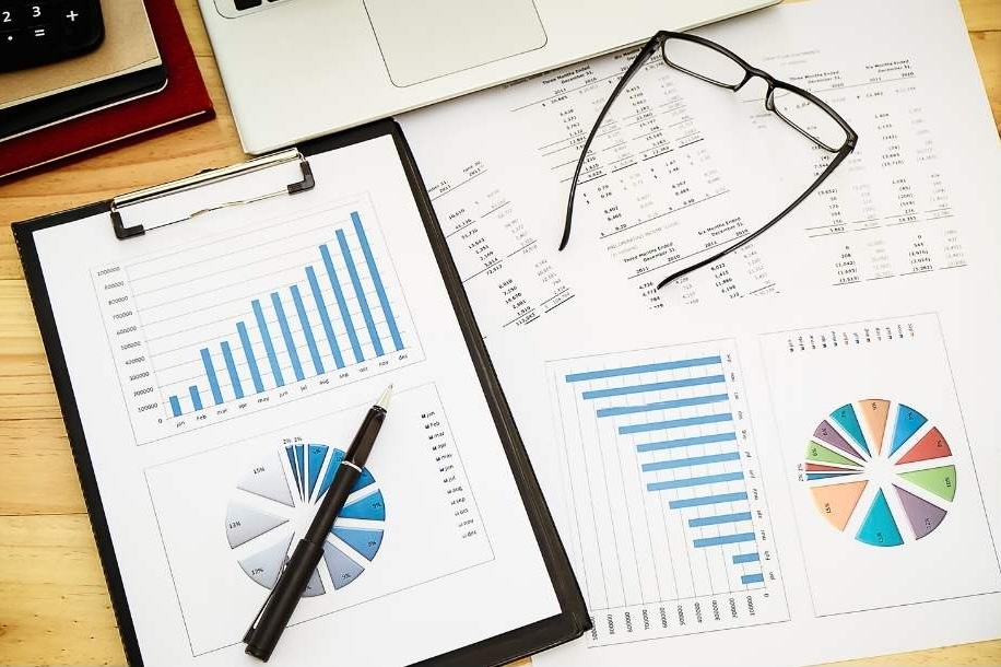 Chart and graphs on a desk next to a pen and a pair of glasses.