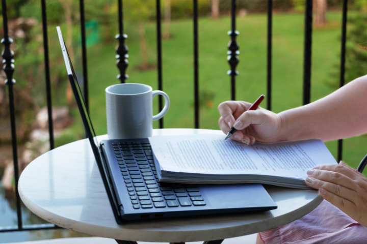 person writing on notepad at table with laptop