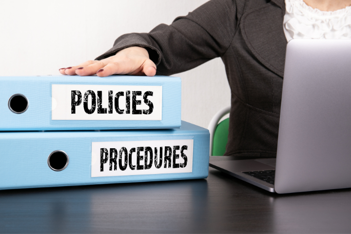 two policy and procedure binders with hand on top