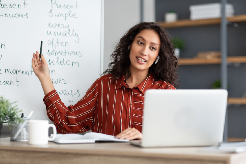Woman speaking into her computer and reaching back towards the whiteboard behind her