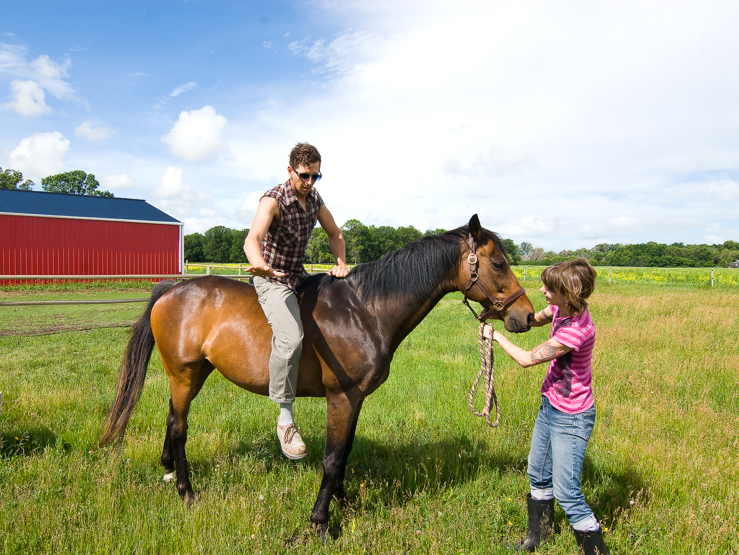 A man sitting on a horse, being helped to get off.